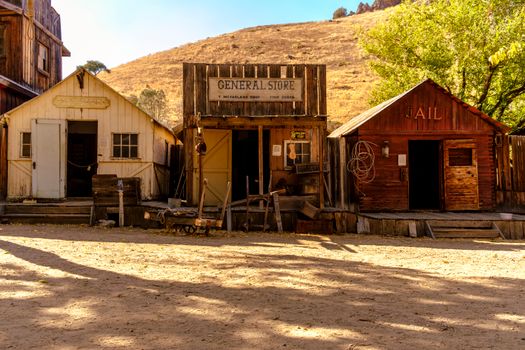 Rustic ghost town with historic general store, old jail, and post office under sunny skies.