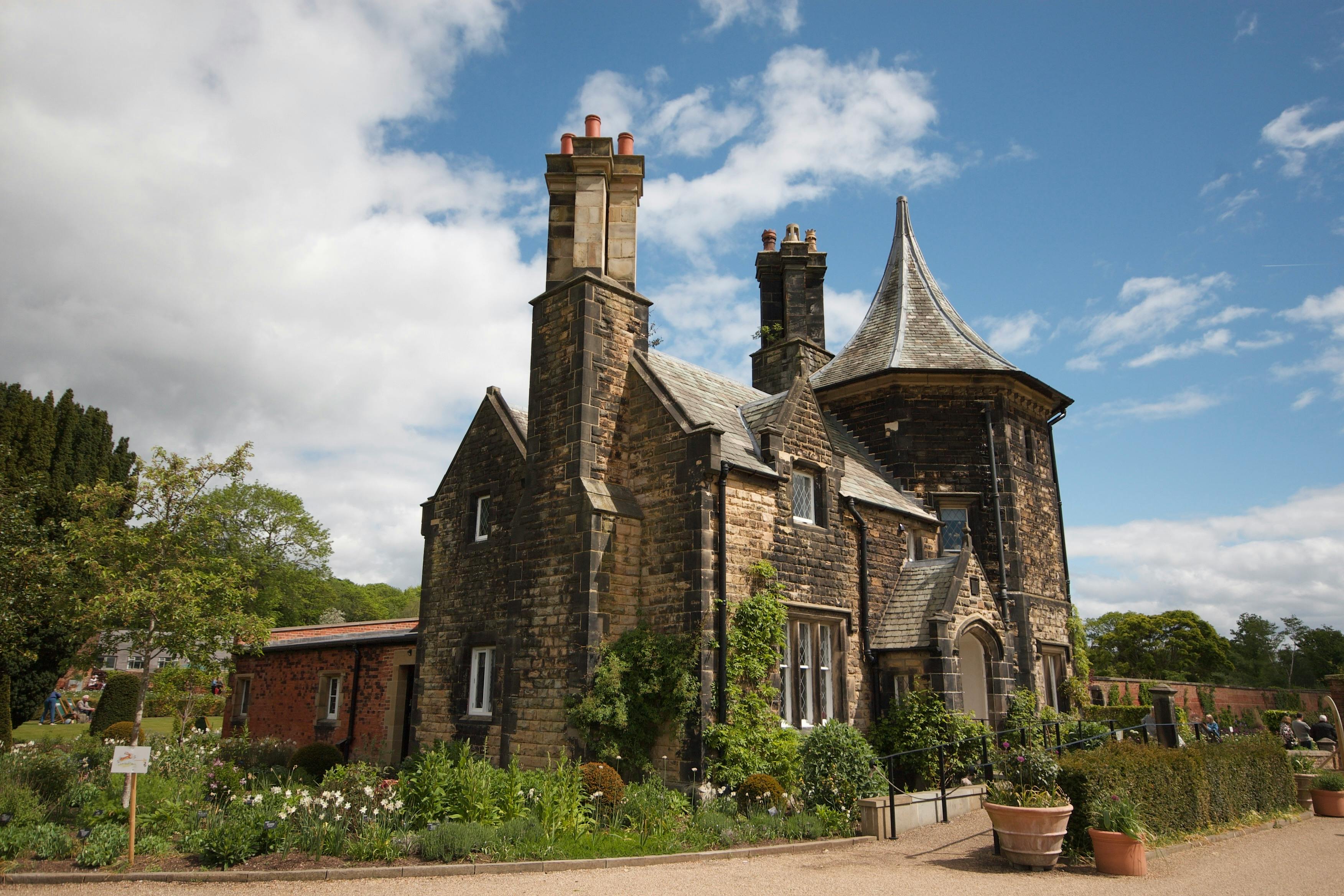Charming Tudor-style house surrounded by lush gardens in Worsley, England, under a bright, clear sky.