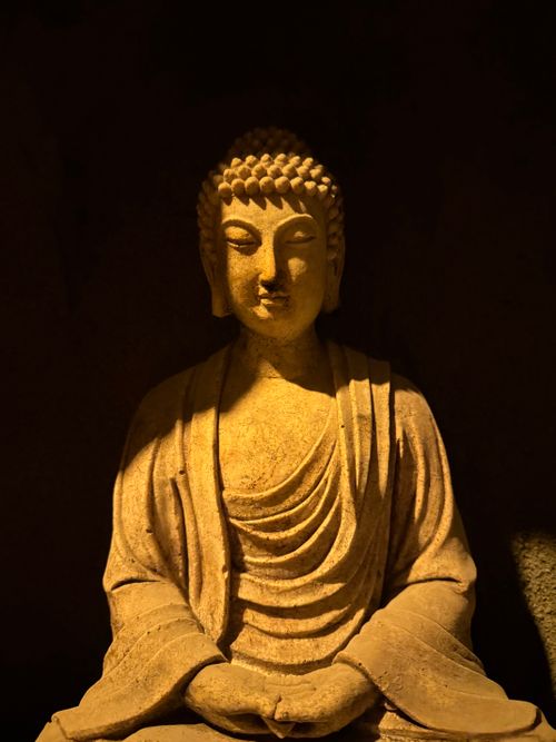 Free Serene Buddha sculpture illuminated by warm, dramatic lighting indoors. Stock Photo