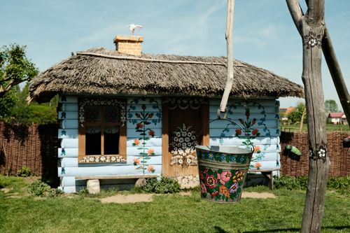 Free Quaint rural house with artistic floral murals, vibrant bucket, and thatched roof. Stock Photo