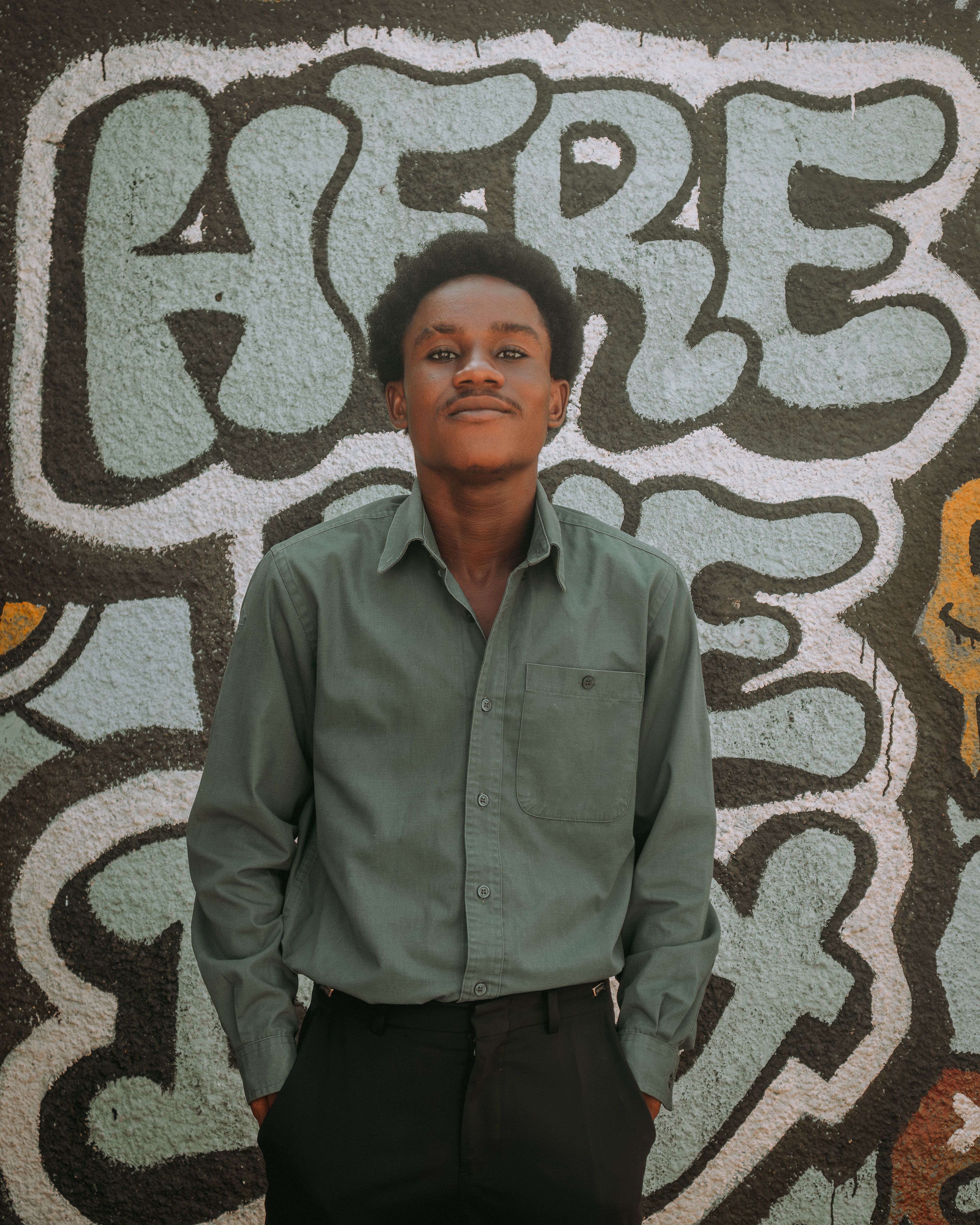 Portrait of a young man in green shirt standing against colorful graffiti wall. Fashion and street art vibe.