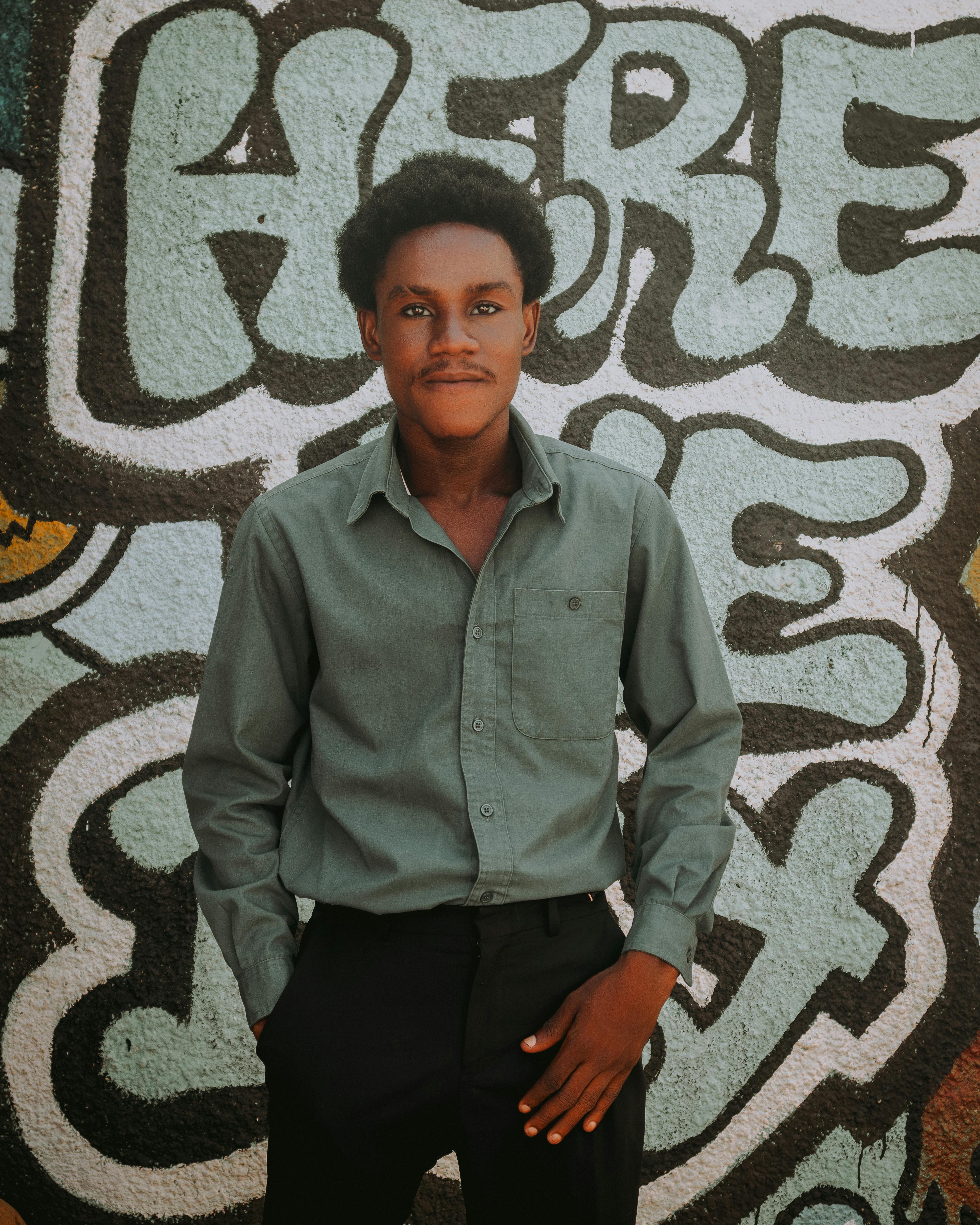 Portrait of a young man standing confidently in front of a vibrant graffiti wall.