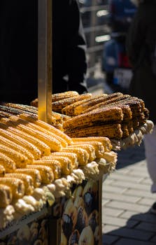 Stall of golden grilled corn on the cob in outdoor market setting.