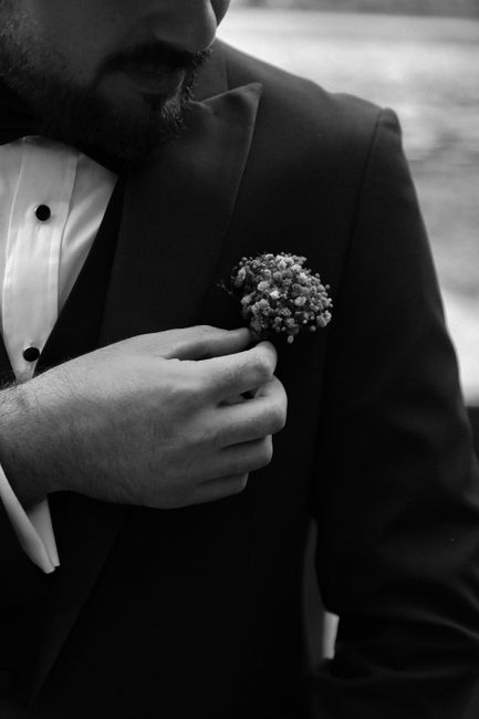 Stylish black and white portrait of a groom adjusting boutonniere. Perfect for classic wedding themes.