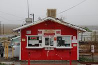 Red roadside shack with an 'Order Here' sign and 'Open' light on a rainy day.