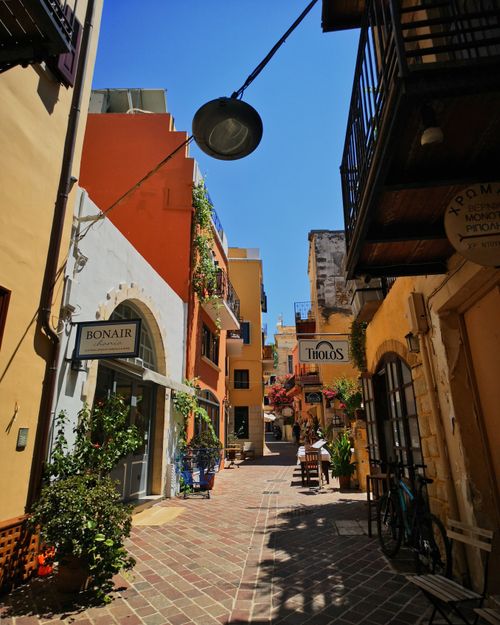 Gratis Esplora una vivace via pedonale nel centro storico di Chania, caratterizzata da edifici colorati e negozi locali. Foto a disposizione