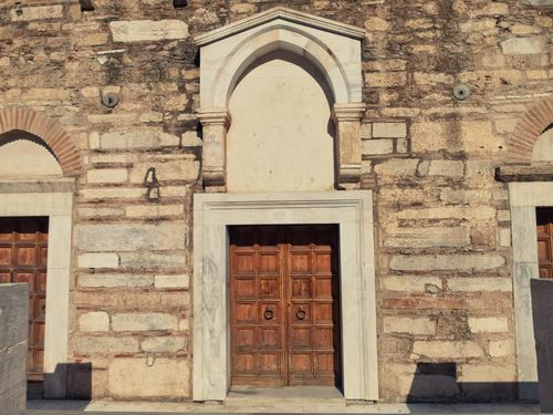 Free Detailed view of a historic stone wall with a central wooden door and arch in Grecia. Stock Photo