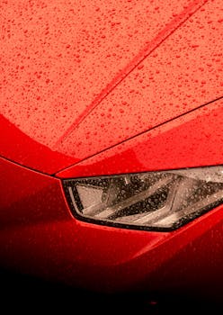 Detailed view of a red sports car hood with raindrops, highlighting sleek design and modern style.