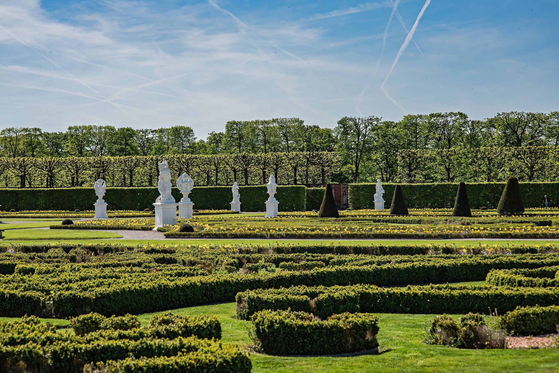 A beautifully manicured garden with white sculptures and trimmed hedges under a clear blue sky in Hannover.