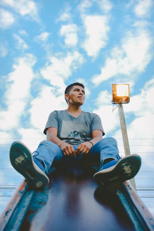 Free A young man sitting on a slide enjoying a bright day with a clear blue sky. Stock Photo