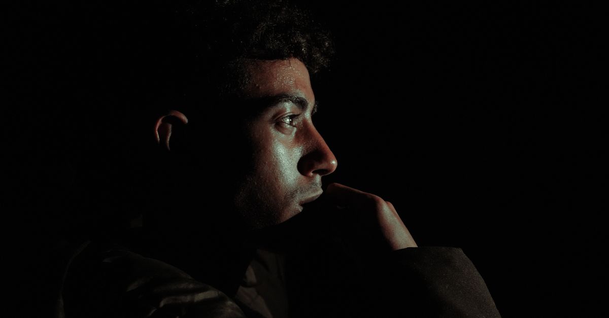 Close-up profile of a man in dramatic side lighting, showing a hooded eye and calm gaze