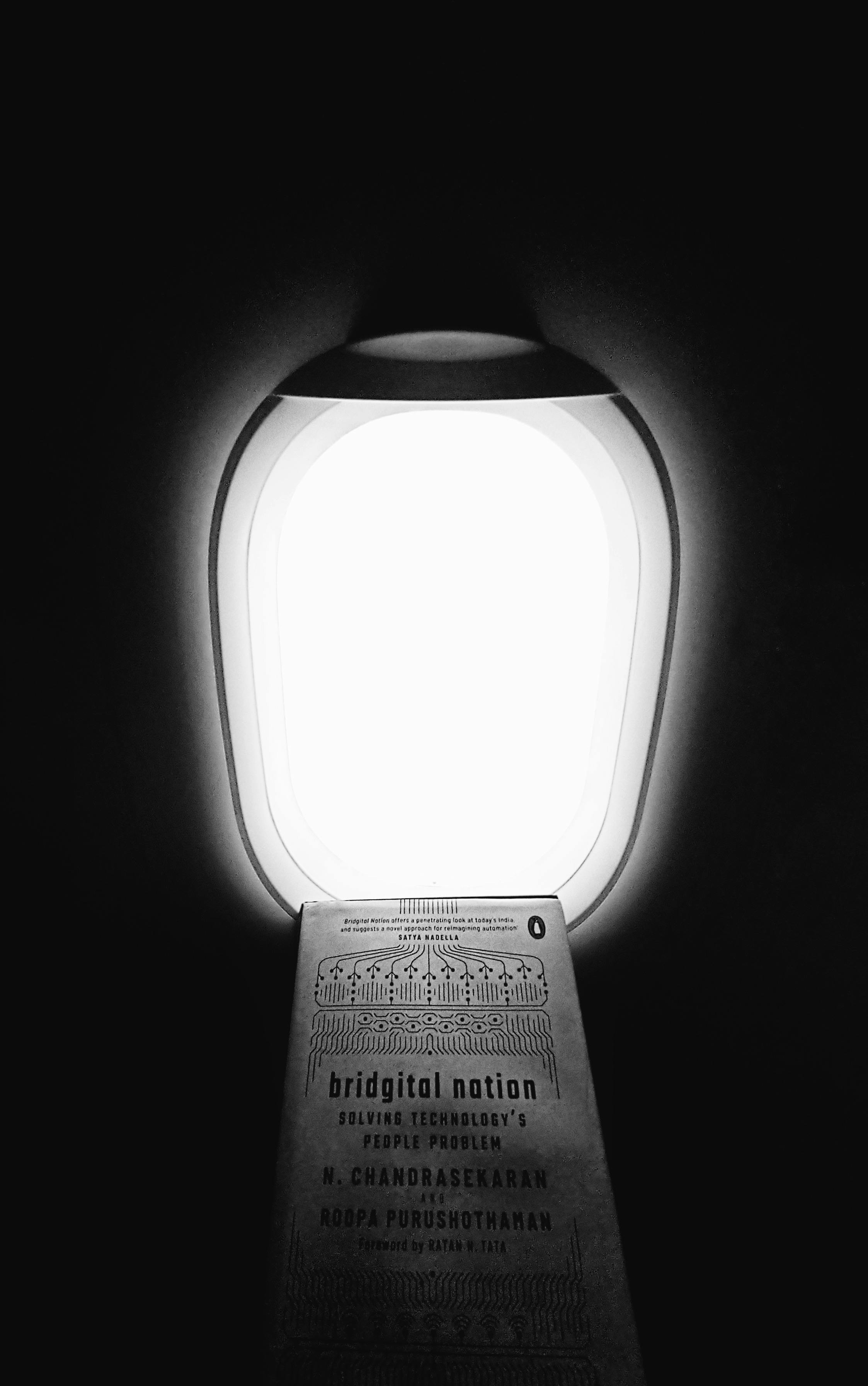 Gratis Foto minimalista in bianco e nero che mostra un libro accanto al finestrino di un aereo. Foto a disposizione