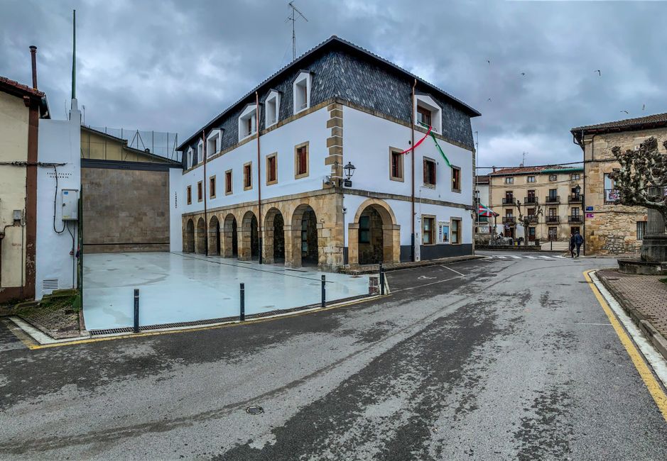 Encantador edificio vasco con arcos y banderas en un paisaje urbano nublado.