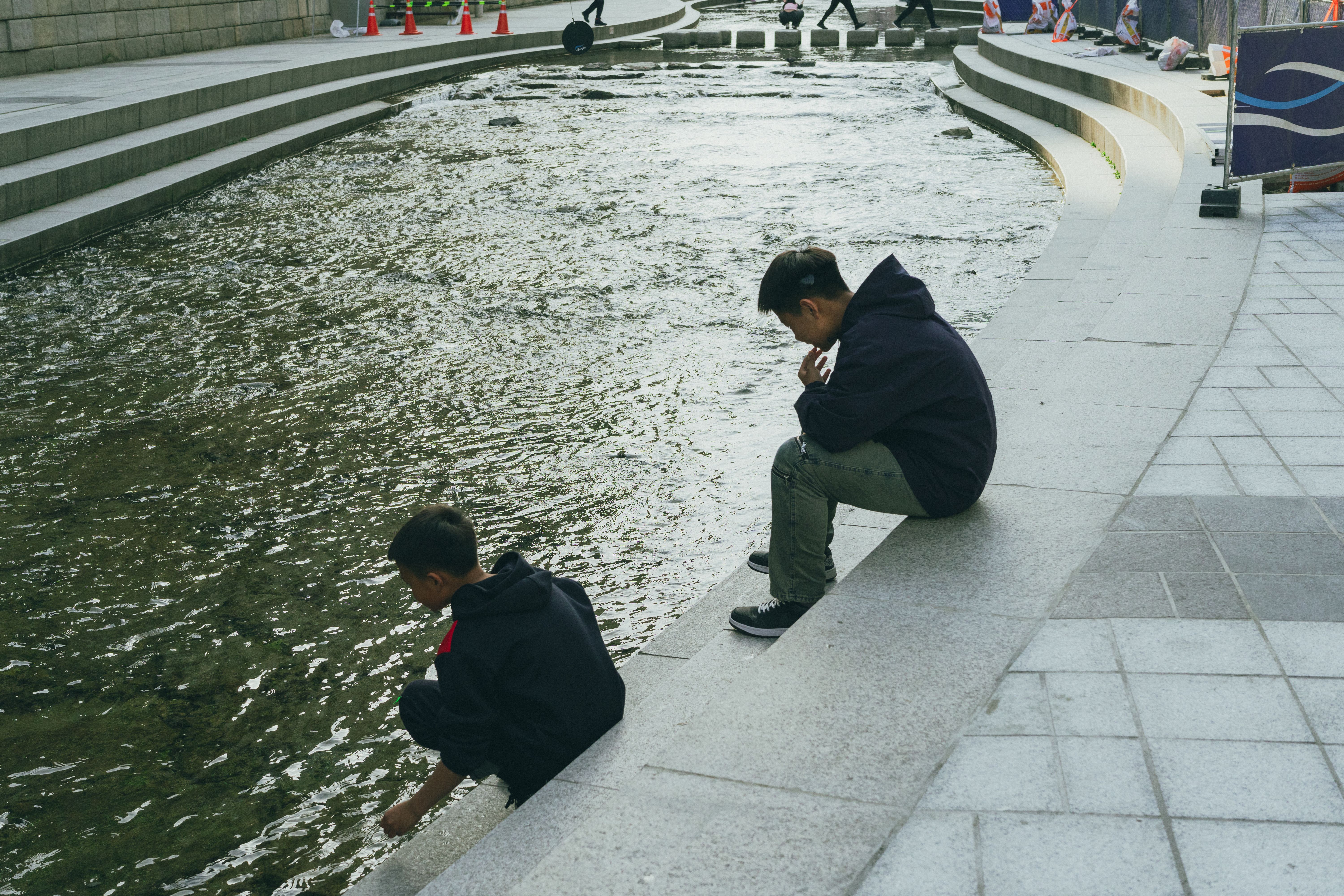 Two boys sitting by Cheonggyecheon Stream in Seoul, capturing a peaceful moment in the city.