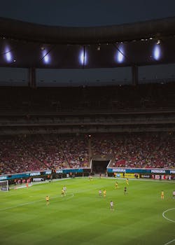 An exciting night football game under bright stadium lights with a large cheering audience.