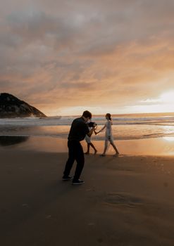 Photographer capturing a couple walking on a picturesque beach at sunset, creating a romantic atmosphere.