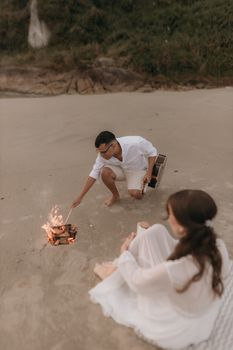 A couple enjoying a romantic evening by the bonfire on a sandy beach.