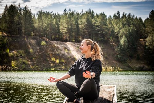 Free Serene moment of a woman practicing meditation near a forest lake in Lithuania. Stock Photo