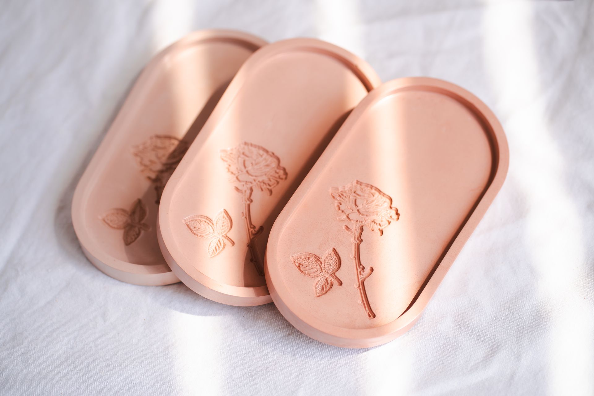 Three pink handmade ceramic trays with embossed rose patterns, perfect for decor.