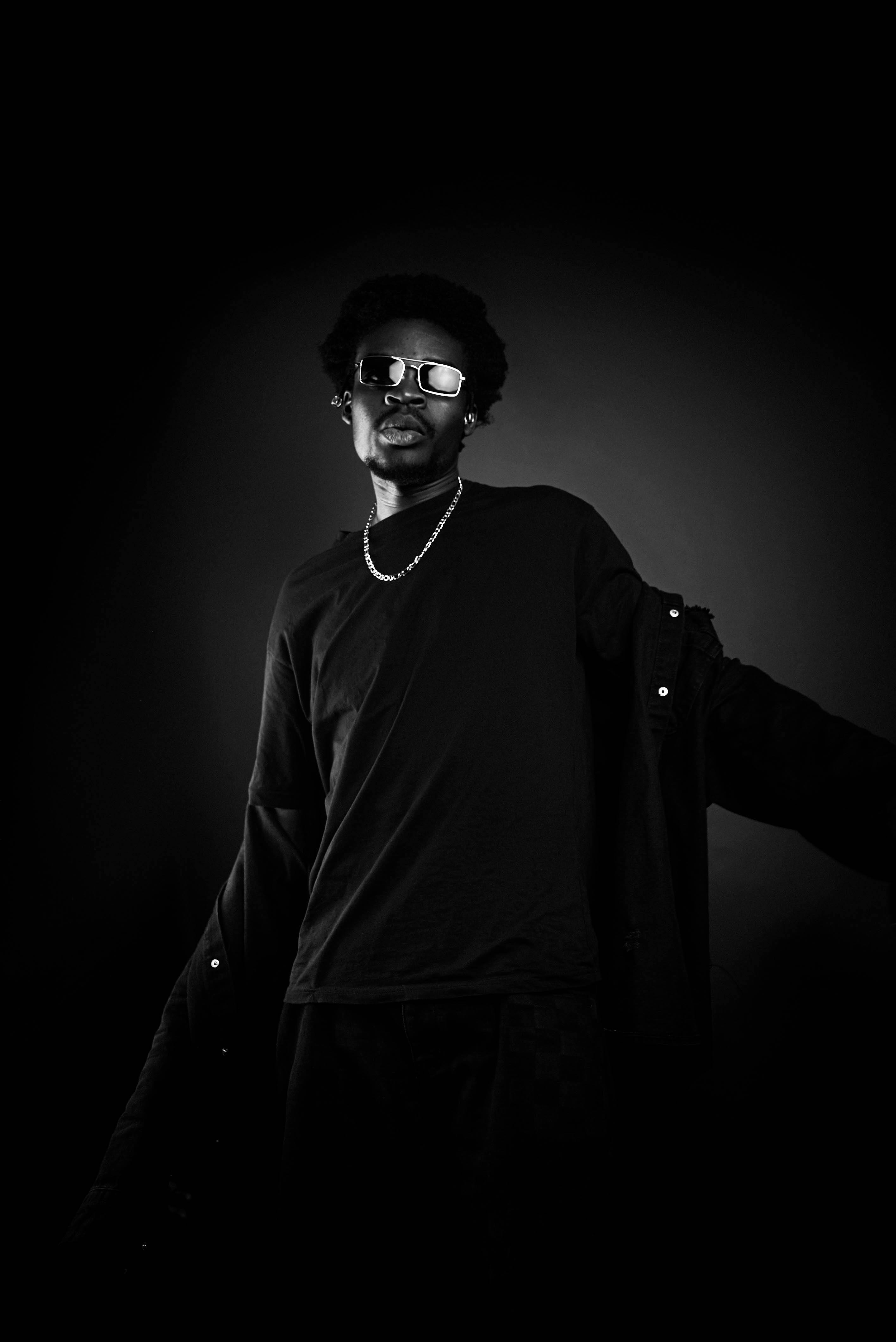 Black and white portrait of a man in sunglasses with afro and chain, exuding cool style.