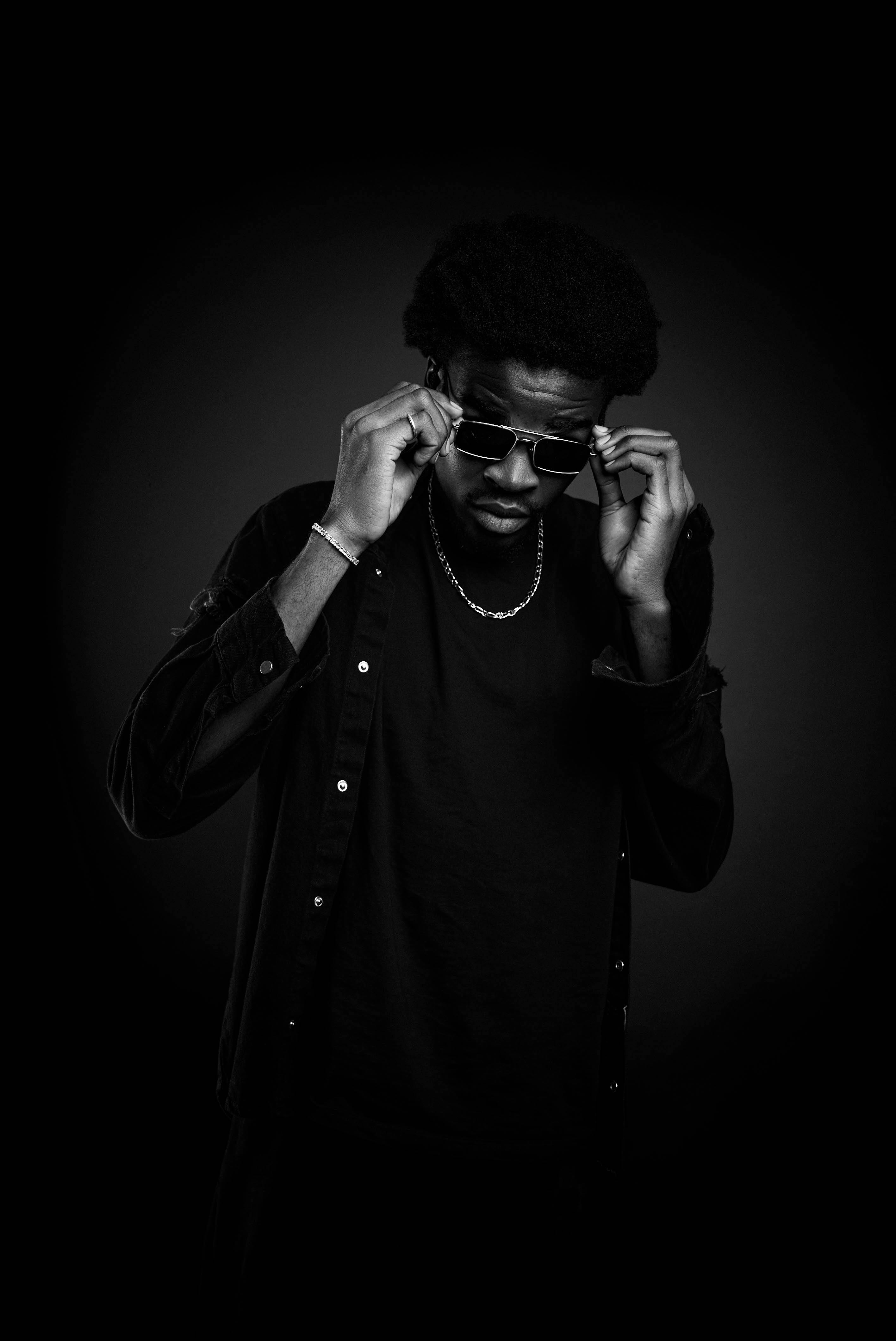 Stylish portrait of a man adjusting sunglasses in a black and white studio shot.