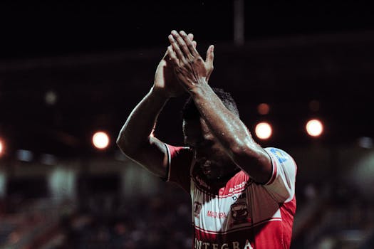 Madura United football player applauding fans during a night game in Bangkalan.