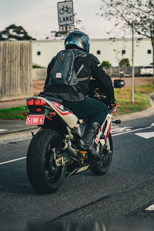 Free A motorcyclist wearing a helmet and backpack rides along a suburban road in Hoppers Crossing, Australia. Stock Photo