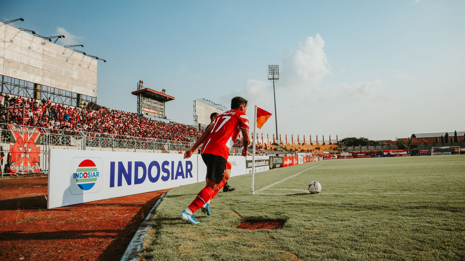 A football player takes a corner kick in a lively Indonesian stadium filled with fans.