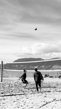 Two people playing beach volleyball under a cloudy sky.