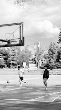 Two teenagers playing basketball on an outdoor court under a cloudy sky.