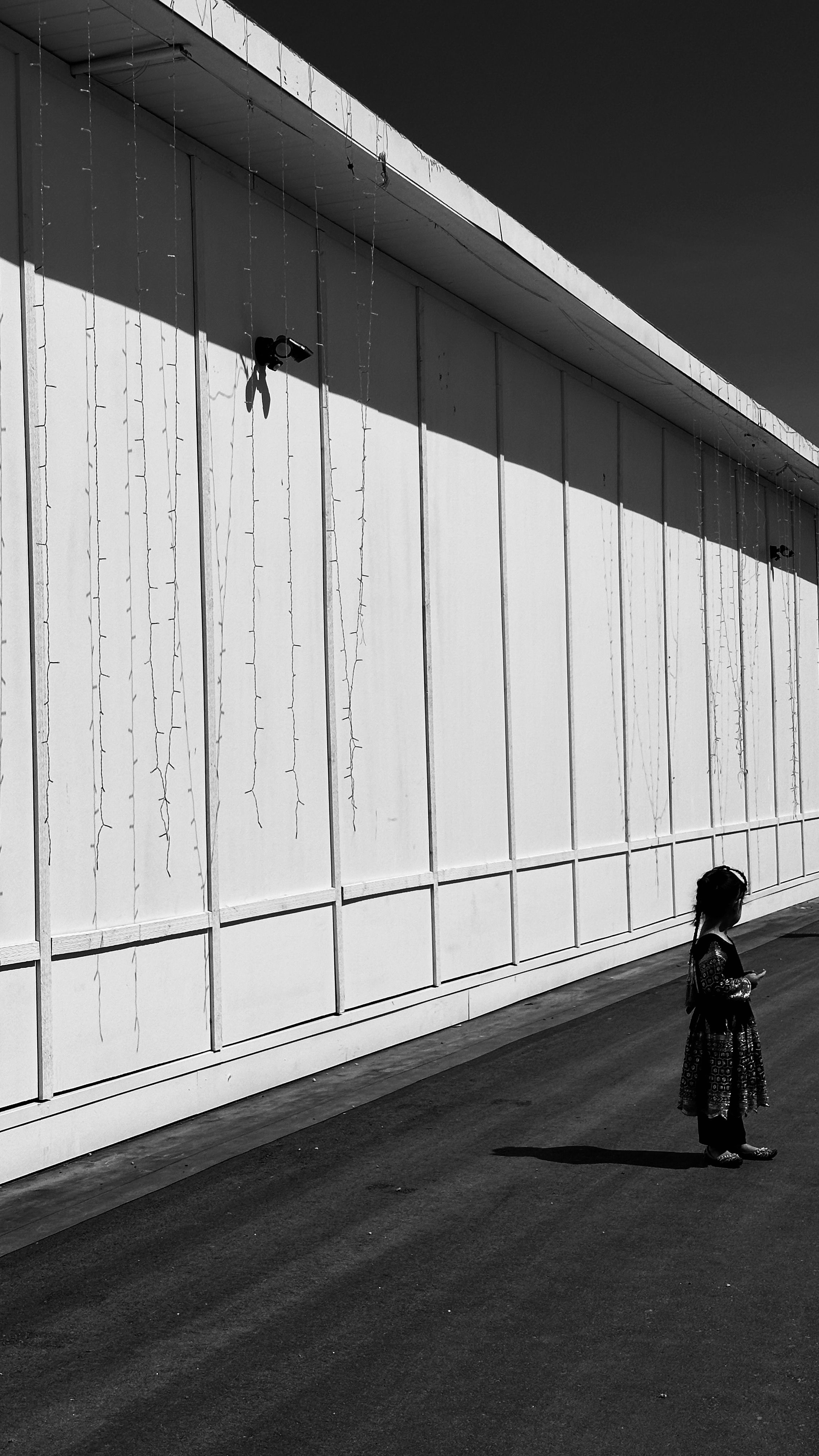 Monochrome image of a solitary child near a stark wall, urban setting.