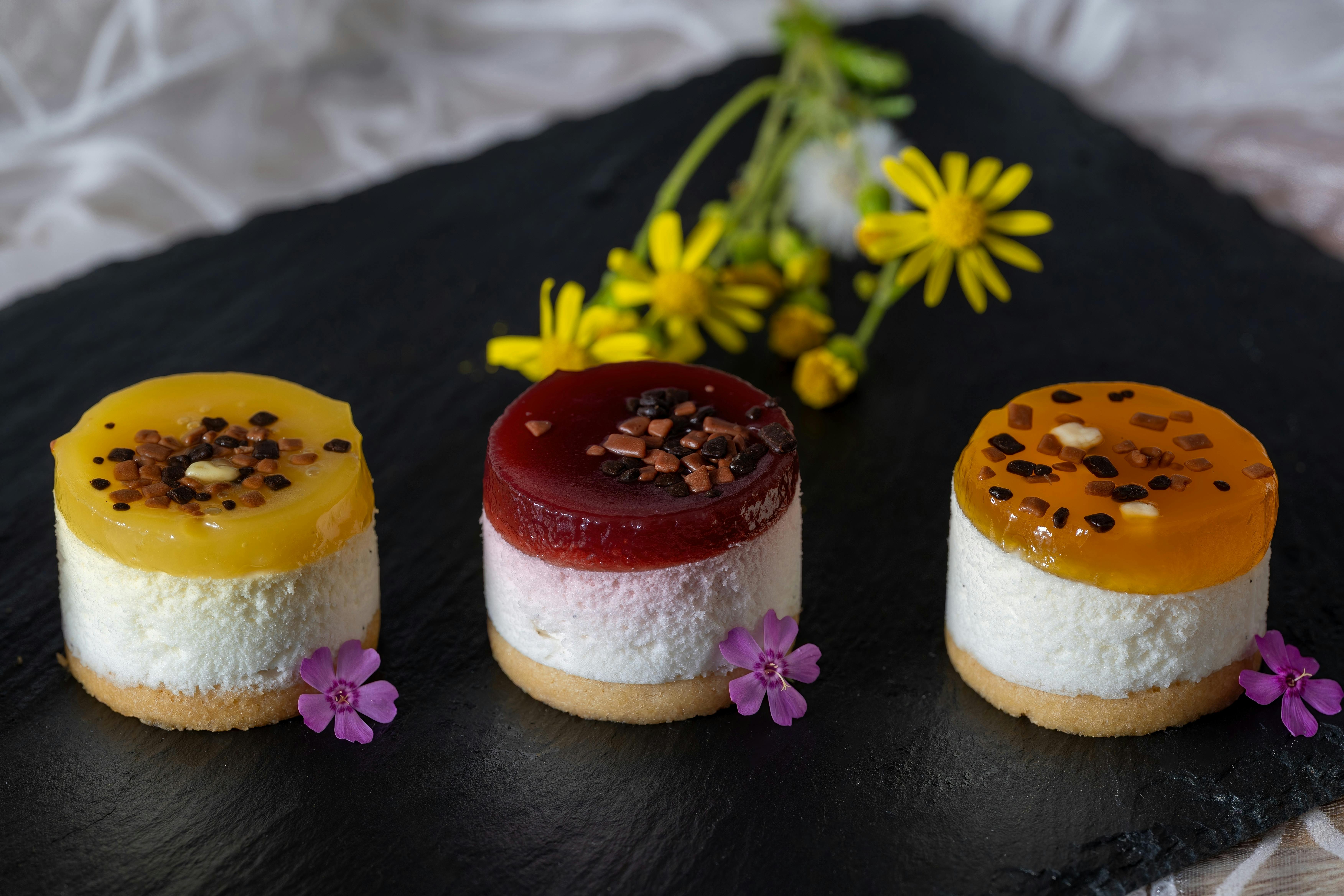 Delight in colorful mini fruit cheesecakes, beautifully garnished with flowers on a dark slate platter.