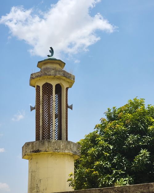 Free A beautiful mosque minaret with crescent detail beside lush green tree under clear sky. Stock Photo