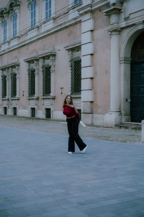 Free A young woman in a red top and black pants walking outside a historic building. Stock Photo