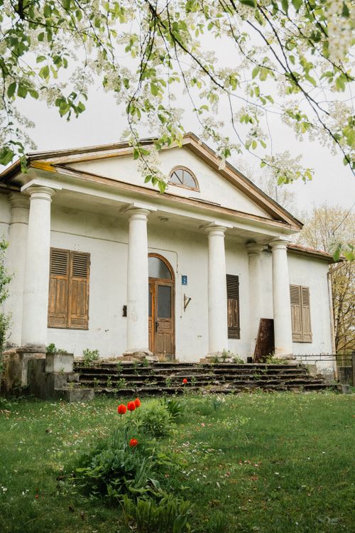 Free Charming historic house with white columns and wooden shutters surrounded by blooming plants. Stock Photo