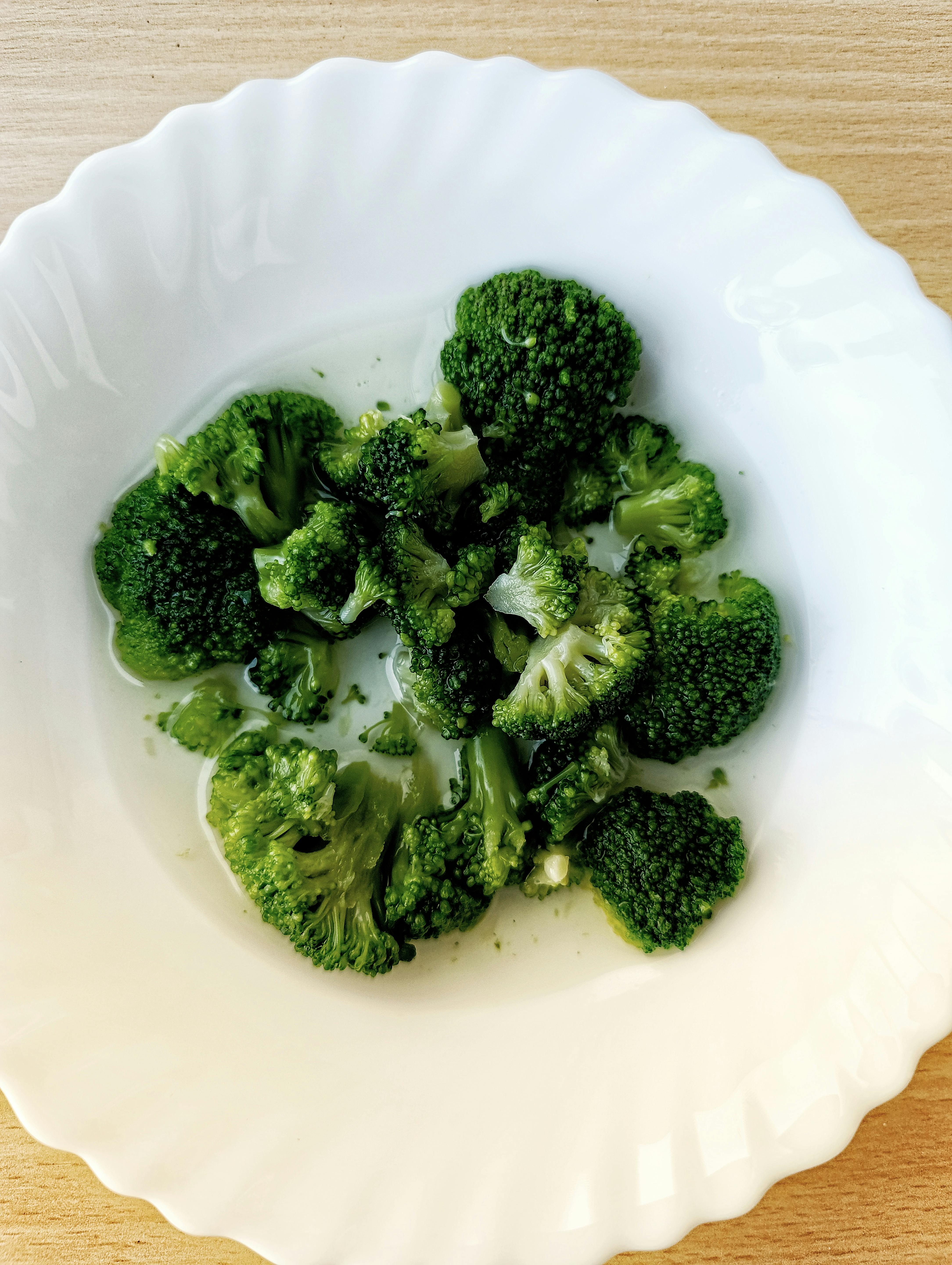 A top view of fresh steamed broccoli on a white plate, emphasizing healthy eating.
