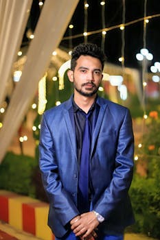 Stylish man in a blue suit posing elegantly during a night event with warm lights.