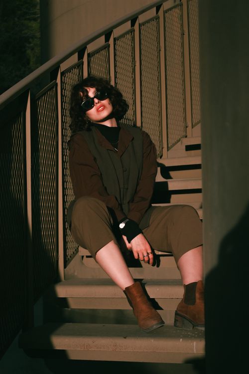 Free Fashionable woman sitting on stairs in sunlight wearing sunglasses and boots. Stock Photo