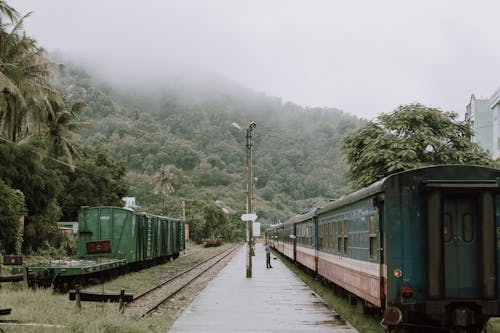 Person Standing  By An Old Train  In A Train Stop Close To A Mountain With Tick Vegetation
