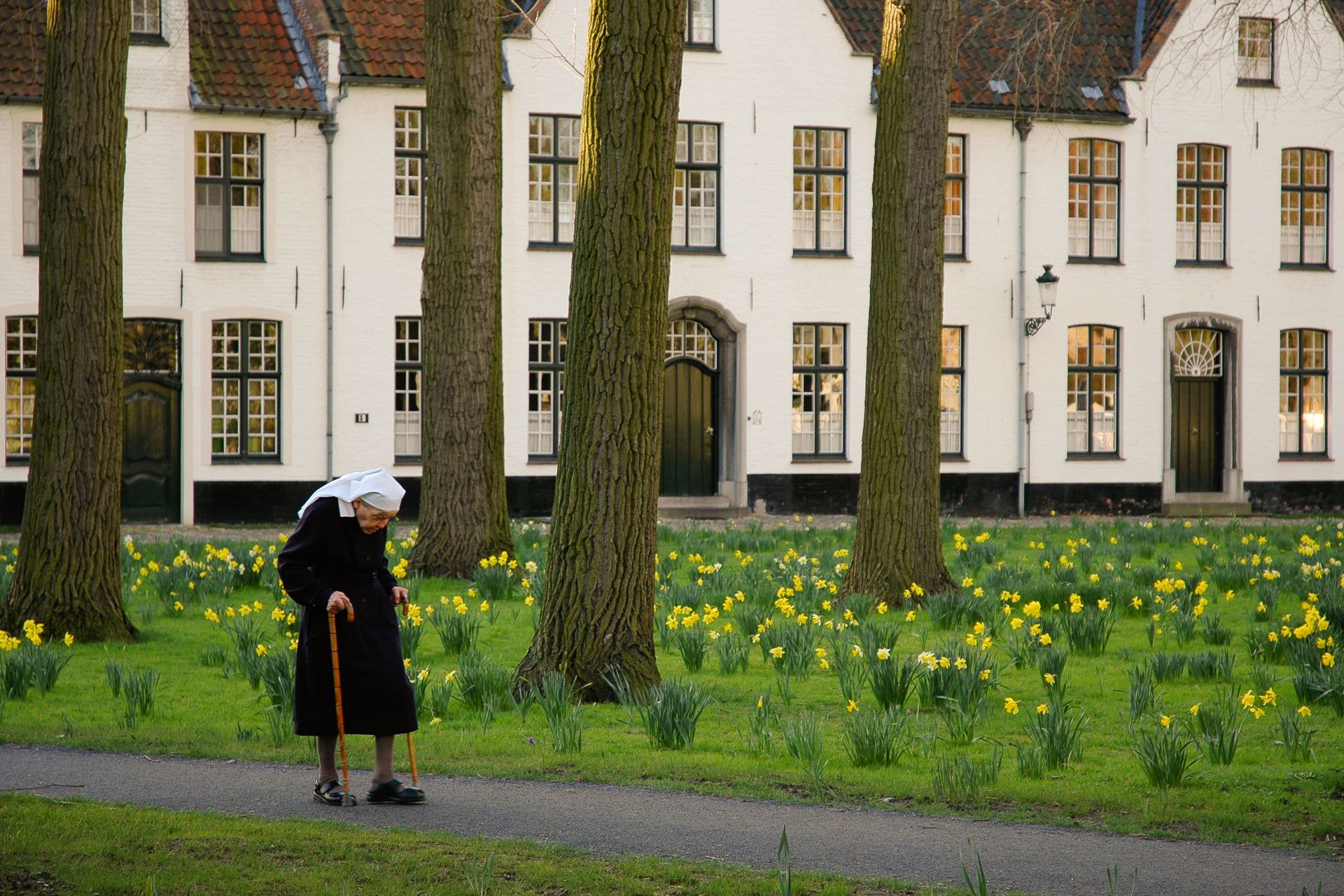 An elderly nun walks through a garden at Begijnhof in Brugge, Belgium.