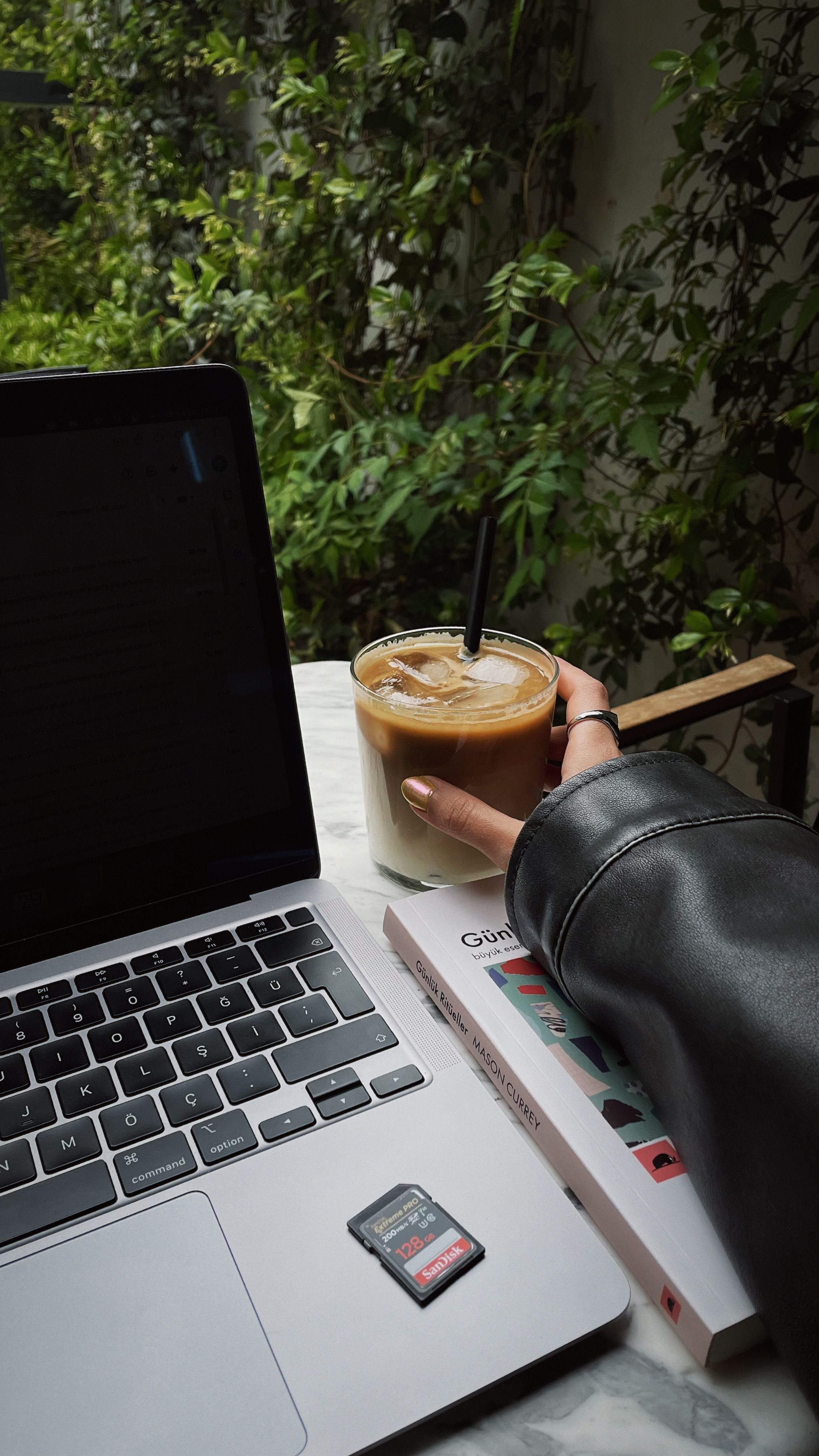 Stylish outdoor cafe setting in Bursa with a laptop, iced coffee, and greenery, capturing a tranquil spring vibe.