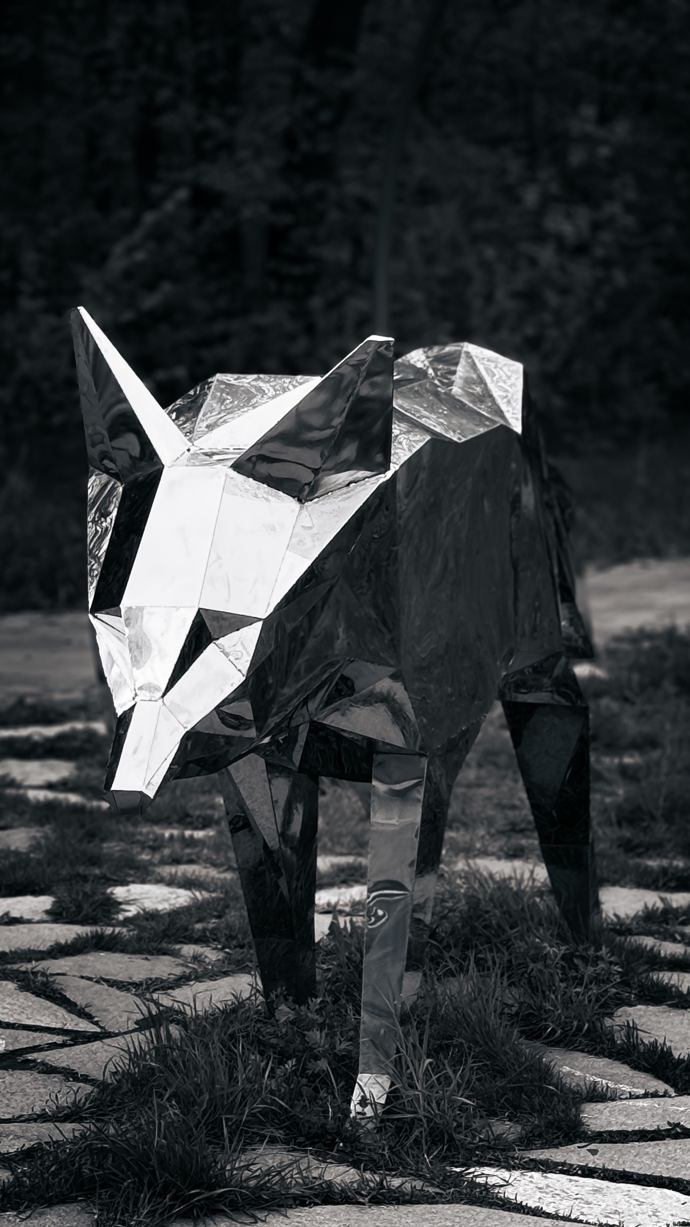 A striking metal wolf sculpture with geometric design in an outdoor forest area.