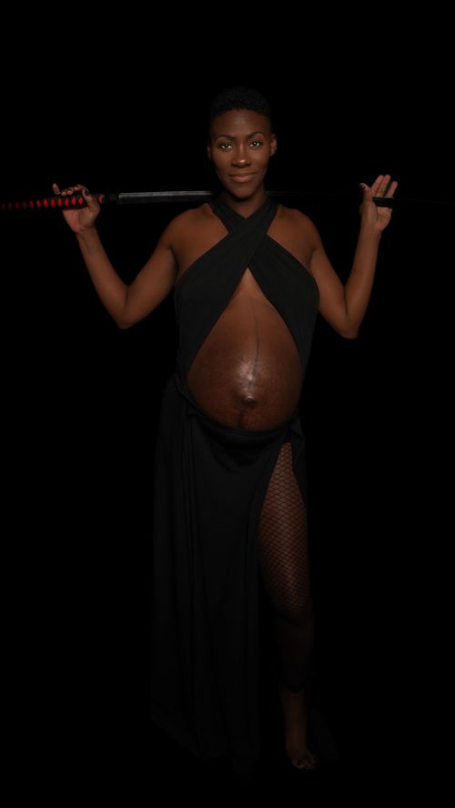Free Pregnant woman in black dress holding sword against dark background. Stock Photo