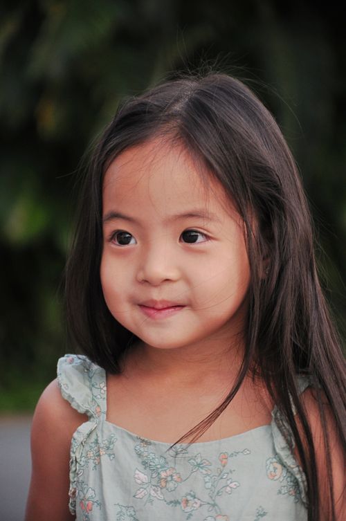 Free A young girl in a floral dress smiles softly in an outdoor setting. Stock Photo