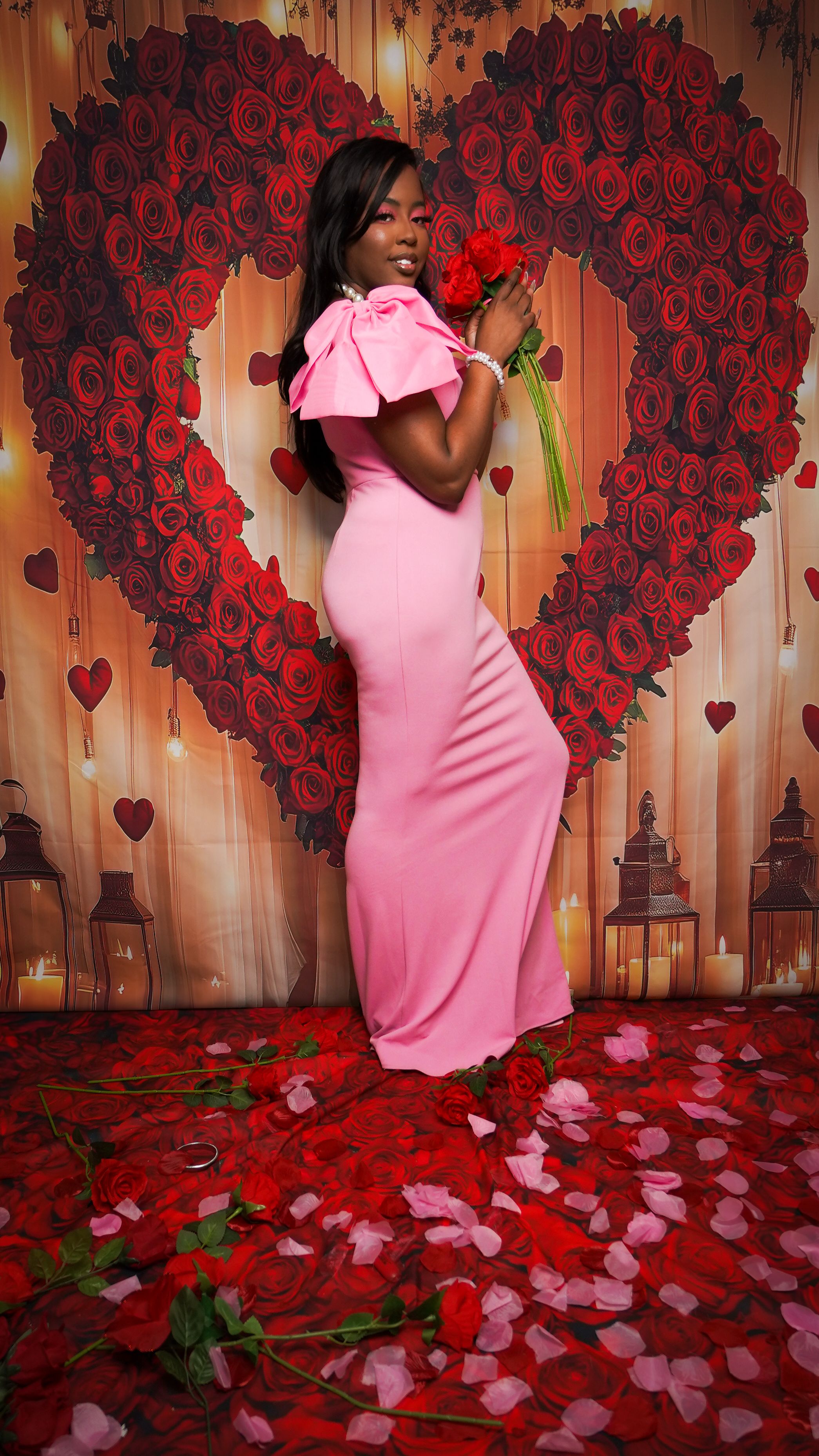 Elegant woman in pink dress holding roses in front of heart-shaped rose backdrop, perfect for romantic themes.