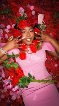 Woman wearing pink dress adorned with red roses and petals, offering a romantic, joyful atmosphere.