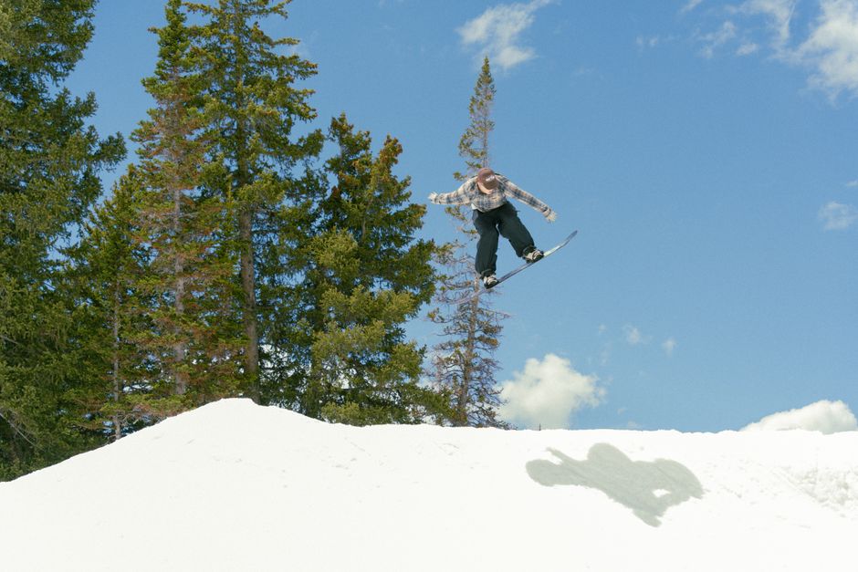 Dynamic action shot of a snowboarder jumping against a blue sky at Brighton Resort, Utah.