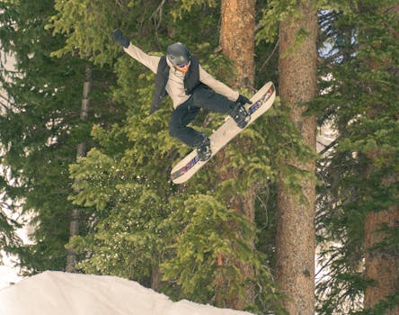 A snowboarder performs an impressive jump surrounded by snow-covered trees at Brighton Resort, Utah.