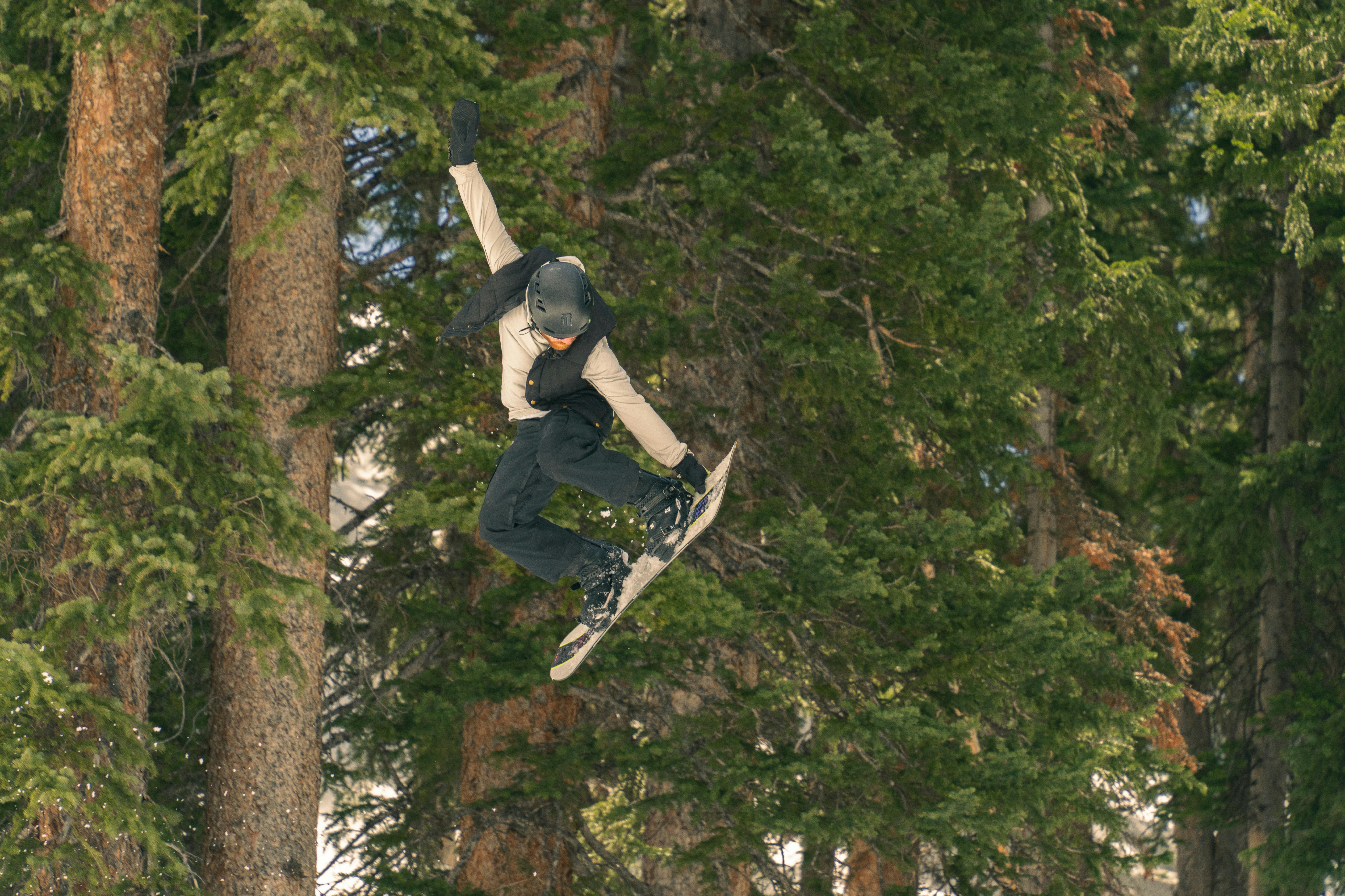 A snowboarder performs an exciting jump amidst lush pine trees in Brighton, Utah.
