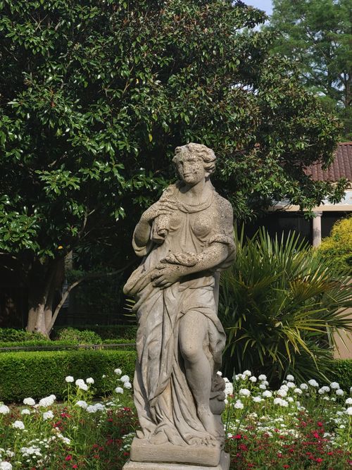Free Classical stone statue amidst vibrant garden flowers and greenery during daytime. Stock Photo
